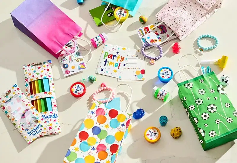 Colourful party bags filled with toys, stickers, slime pots, bracelets, and party favours arranged on a table.